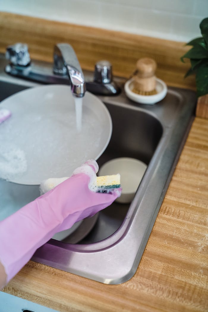 Close-up of a person washing dishes with pink rubber gloves at a kitchen sink.